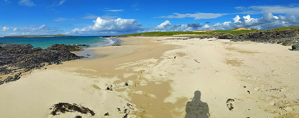 Panoramic picture of a beach in the sun, a small island in the distance
