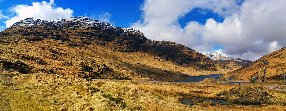 Panoramic picture of snow covered hilltops above a loch at the Rest and Be Thankful