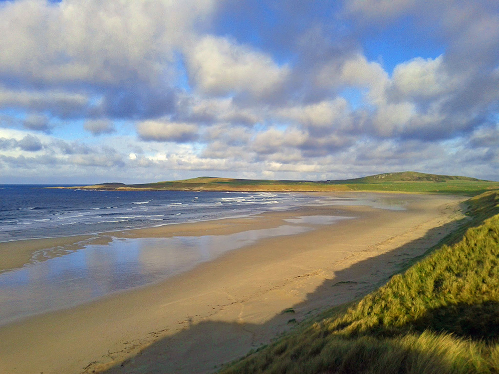 Picture of a wide sandy beach in a bay, seen from dunes above the beach