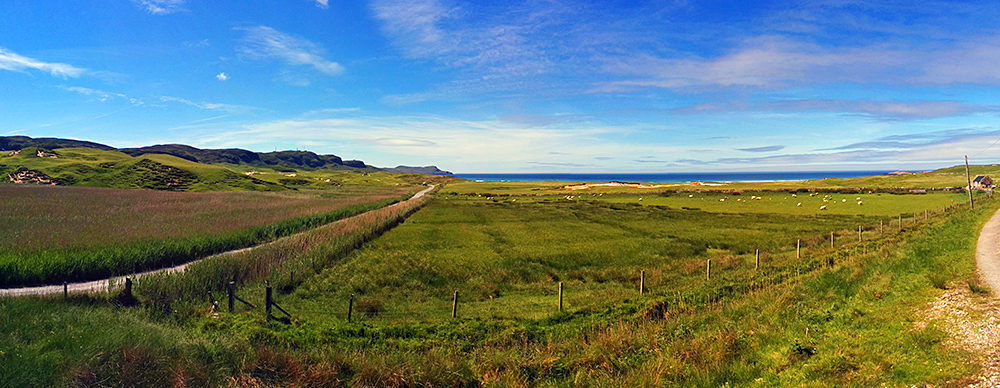 Panoramic picture of a view over a coastal landscape with a track leading to a beach