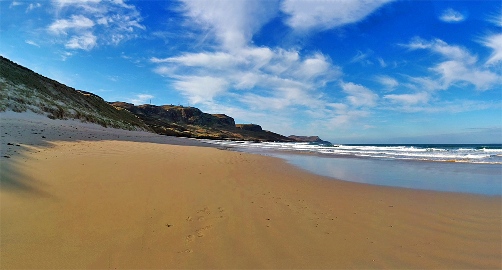Panoramic picture of a row of dunes towering over a beach in a bay
