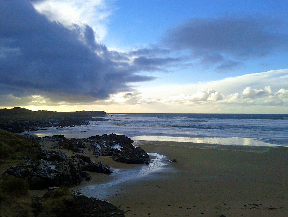 Picture of bay with cliffs and a beach, a big dark cloud blocking the afternoon sun