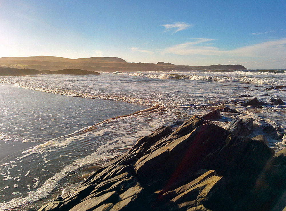 Picture of waves rolling into a bay with a beach in November sunshine