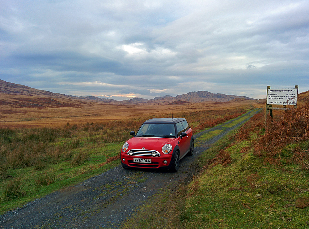 Picture of a car stopped on a rough road in a remote landscape next to a sign with distances