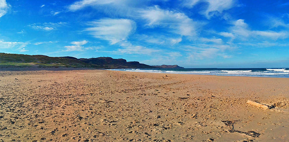 Panoramic picture of a beach with feathery clouds in the sky