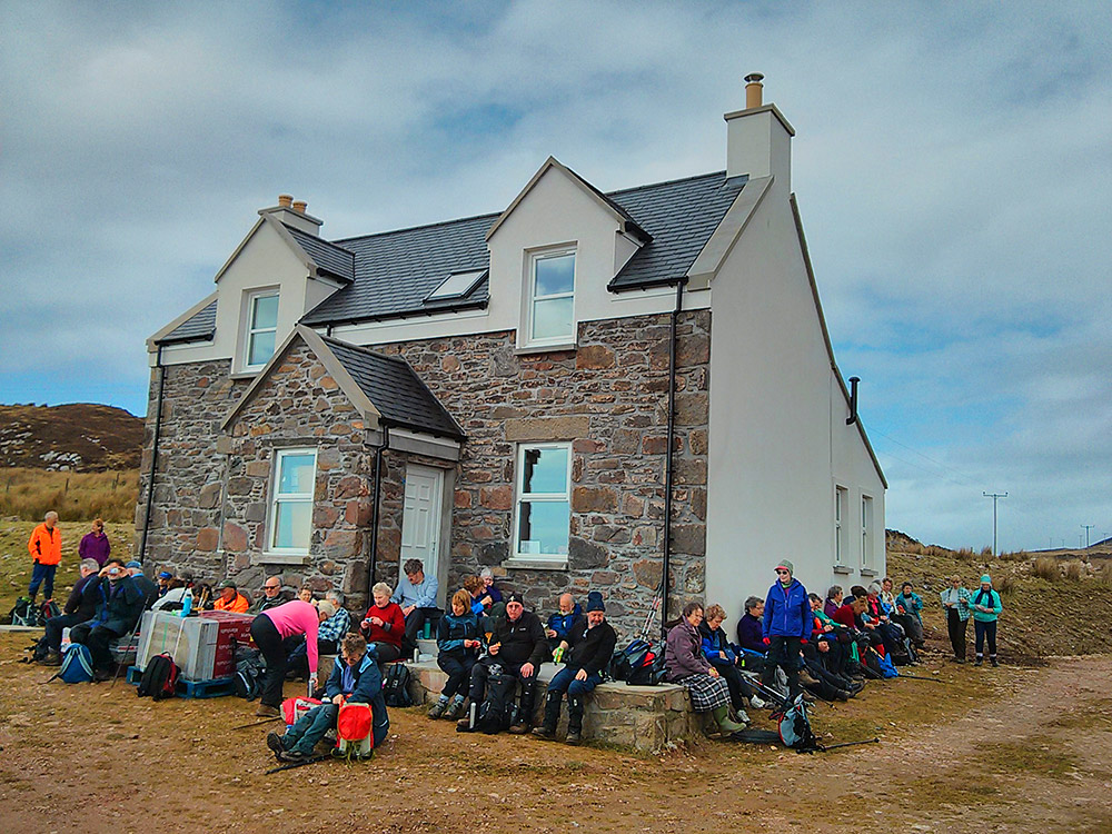 Picture of a large group of walkers having lunch around a house being renovated