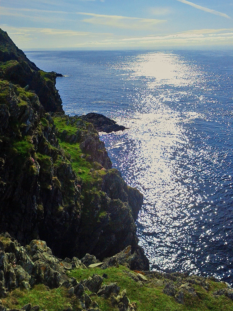Picture of steep cliffs in bright sunshine reflecting on the water