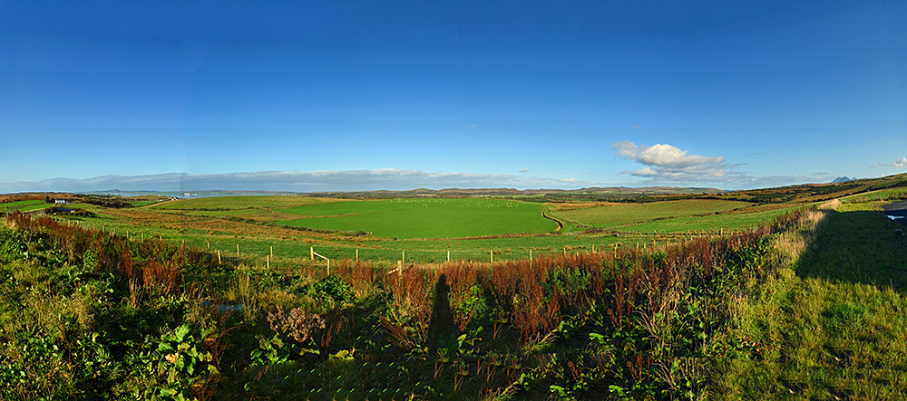 Panoramic picture of a view over a varied landscape with a sea loch, fields and woodland on a sunny morning