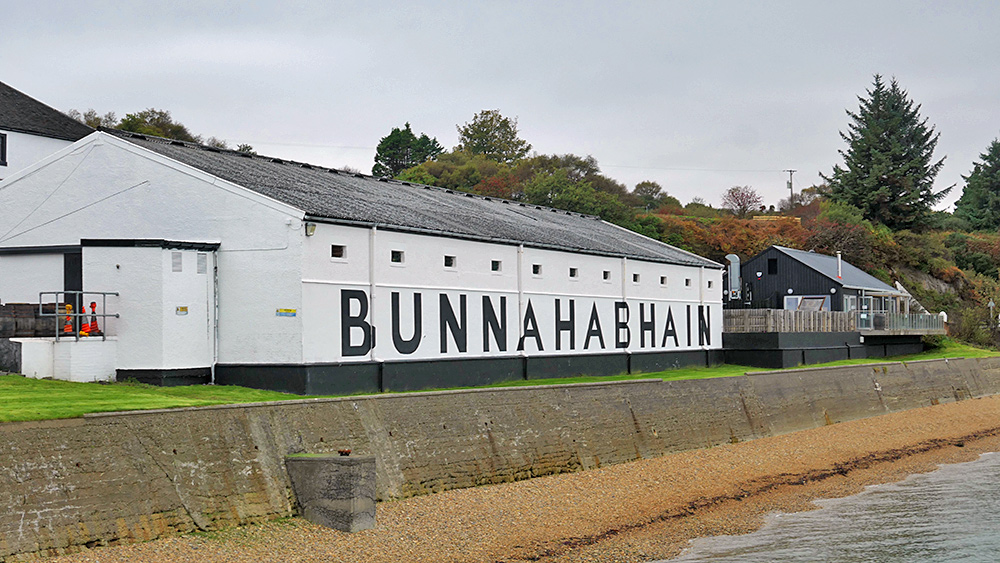 Picture of a whitewashed warehouse with Bunnahabhain lettering, next to it a purpose built visitor centre with a balcony