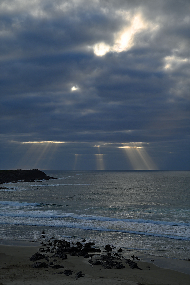 Picture of sun rays breaking through clouds over a coast with rocks and beach