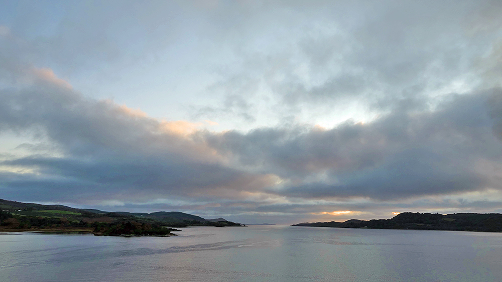 Picture of a view out over a sea loch from a ferry leaving on a partially cloudy October evening