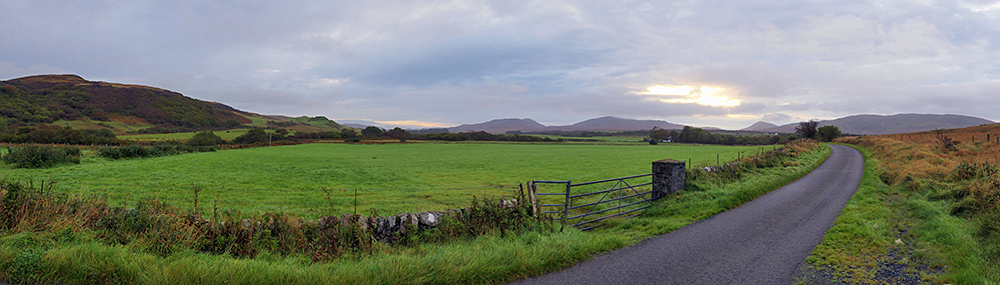 Panoramic picture with a view from a road through a glen on a cloudy morning
