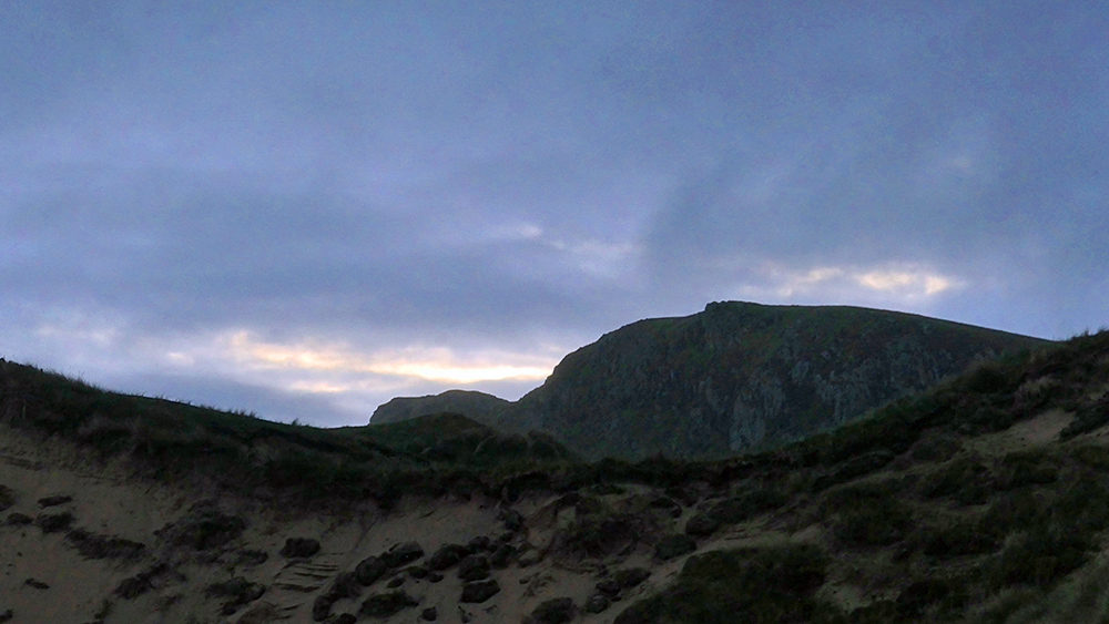 Picture of some dunes with some rocky crags behind them under dark September morning clouds