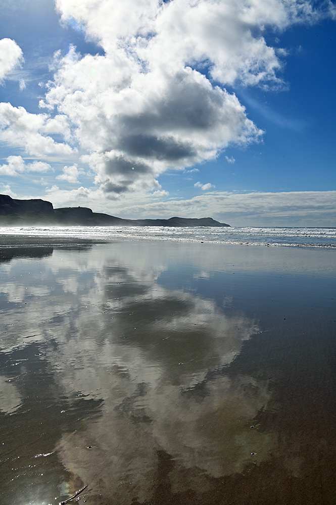 Picture of dramatic September clouds over a bay and beach reflecting on the wet beach