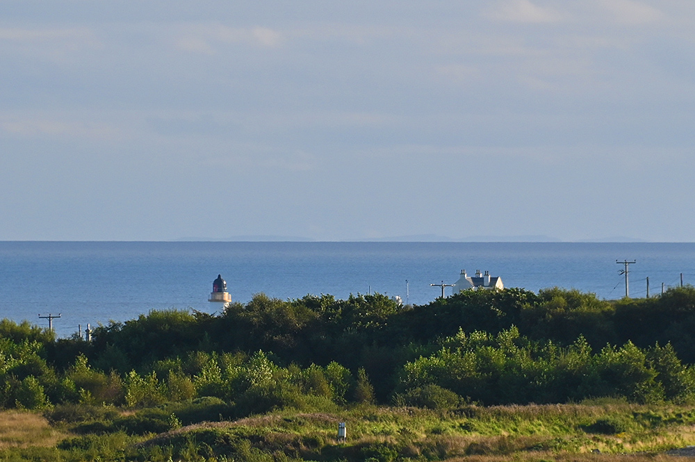 Picture of a lighthouse seen from the distance, half hidden behind trees