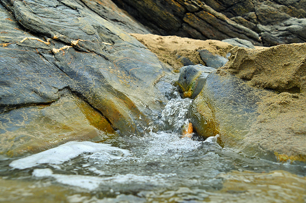 Picture of a tiny waterfall running across a beach with some rocks