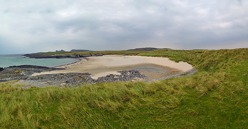 Panoramic picture of a small beach on a coast with dunes and cliffs