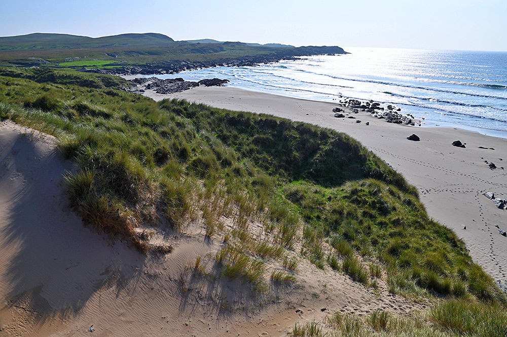 Picture of a bright sunny view from the top of a dune over a bay with a beach and cliffs