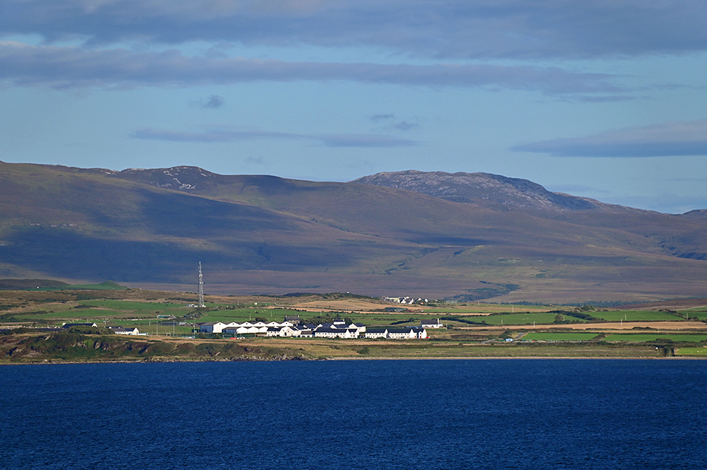 Picture of some distillery warehouse and a new housing development seen across a sea loch