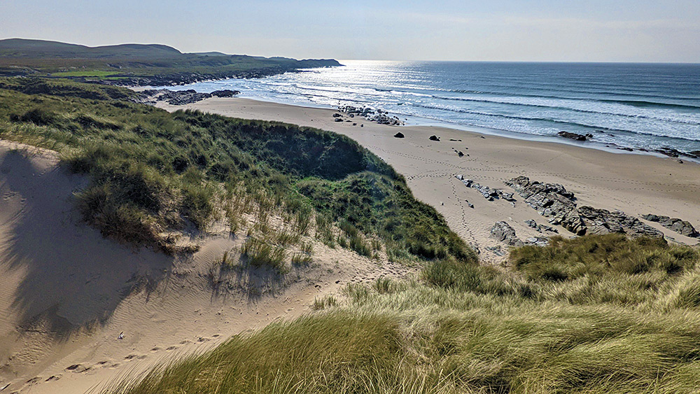Picture of a view from the top of a dune over dunes and a beach at a wide bay