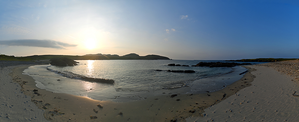 Panoramic picture of a sunset over a small bay with a sandy beach