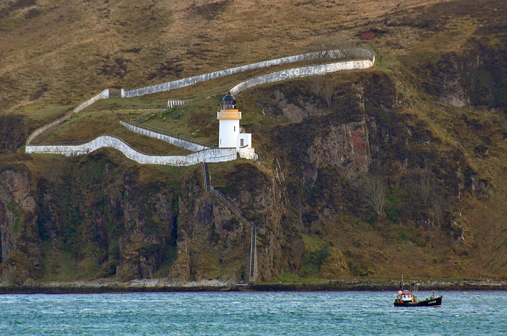 Picture of a fishing boat passing below a lighthouse on some steep cliffs