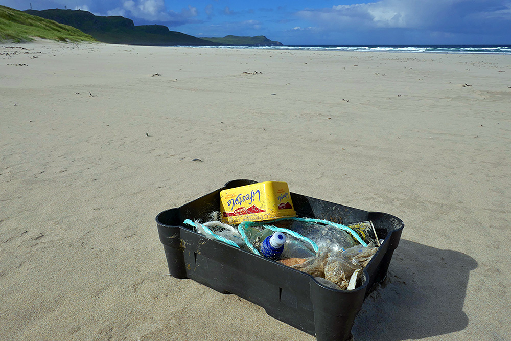 Picture of a box with the findings from a beach clean with the beach in the background