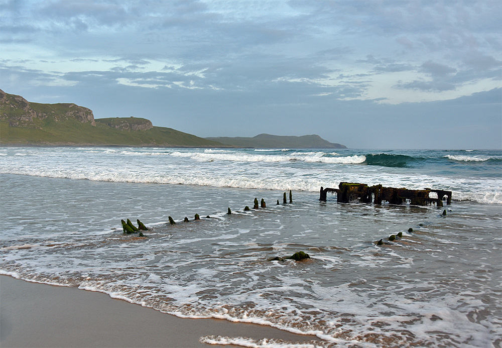 Picture of a wreck on a beach with the waves/surf from the bay rushing in around it