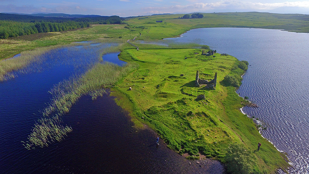 Picture of an island with some old ruins on it in in a loch in the summer morning sunshine