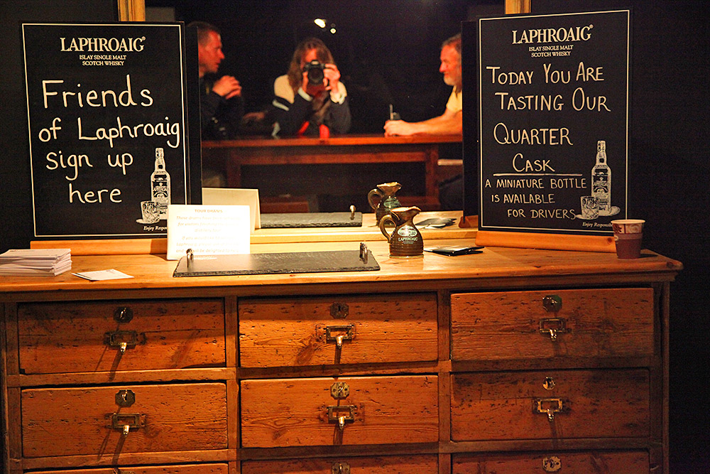 Picture of a wooden cabinet at a distillery tasting room, a mirror with people visible on top