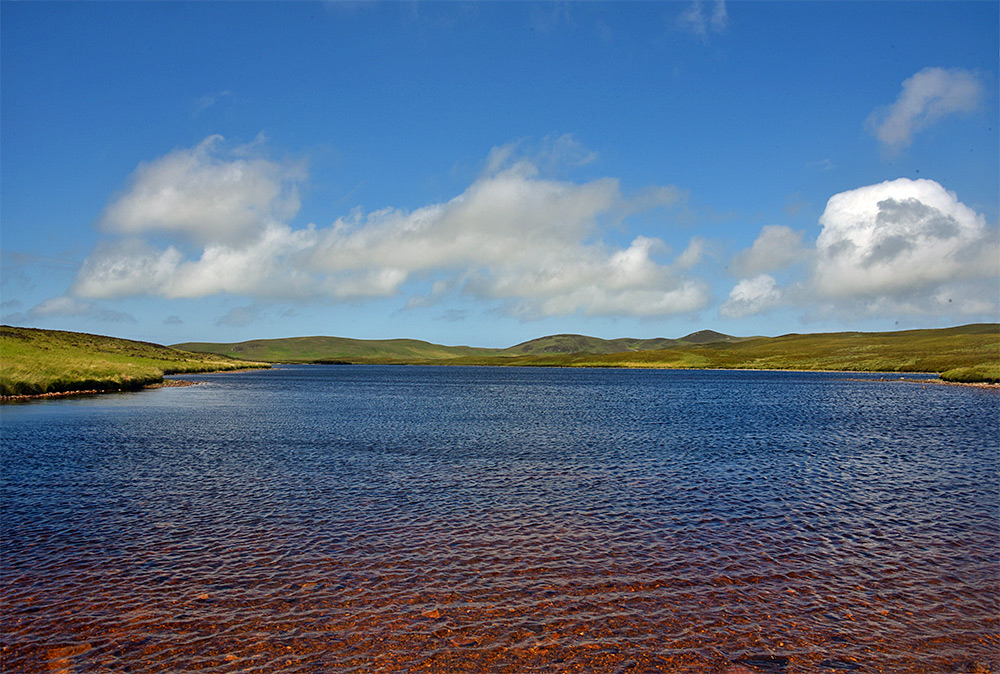 Picture of a view over a freshwater loch on a sunny June day, some light clouds in the distance