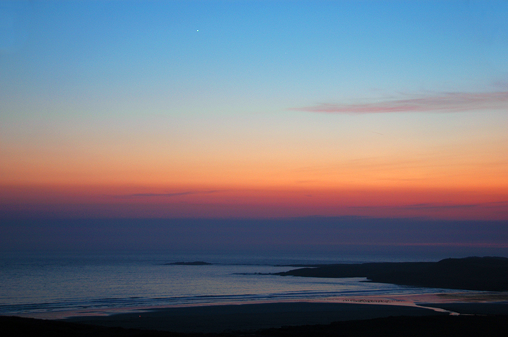 Picture of a view over a bay with a beach from some high dunes during the gloaming just after sunset