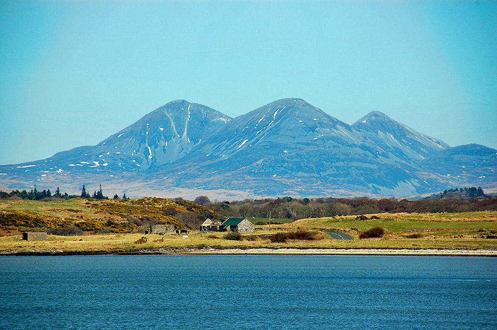 Picture of three mountains towering over an old house (half ruin) at the shore of a sea loch