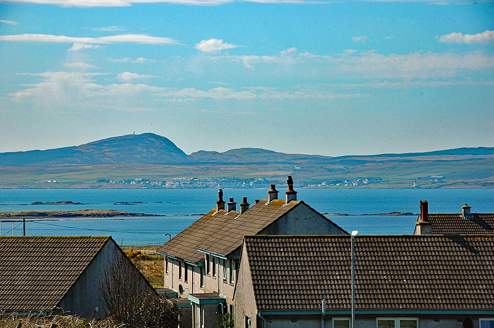 Picture of a view across some roofs of a coastal village over a sea loch to another coastal village
