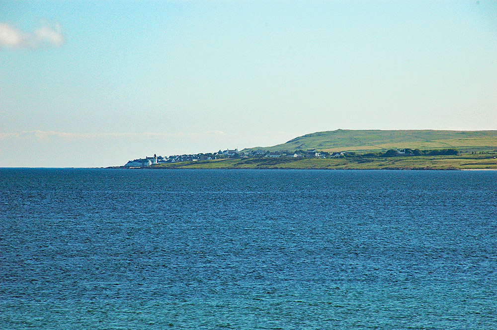 Picture of a coastal village with a lighthouse seen across a sea loch