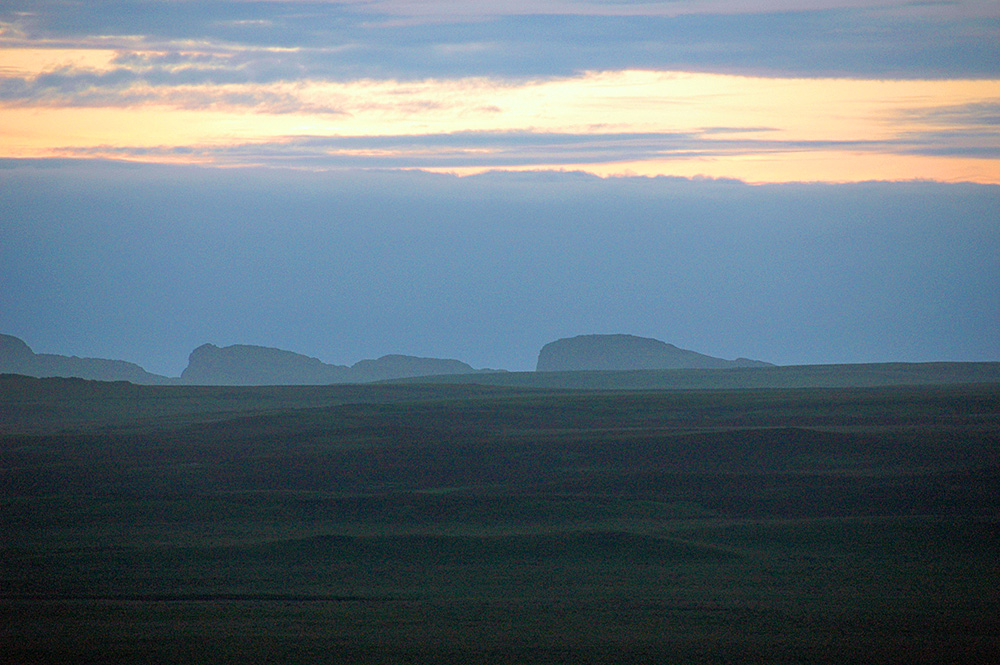 Picture of a hilly landscape with distant cliffs on a misty June evening