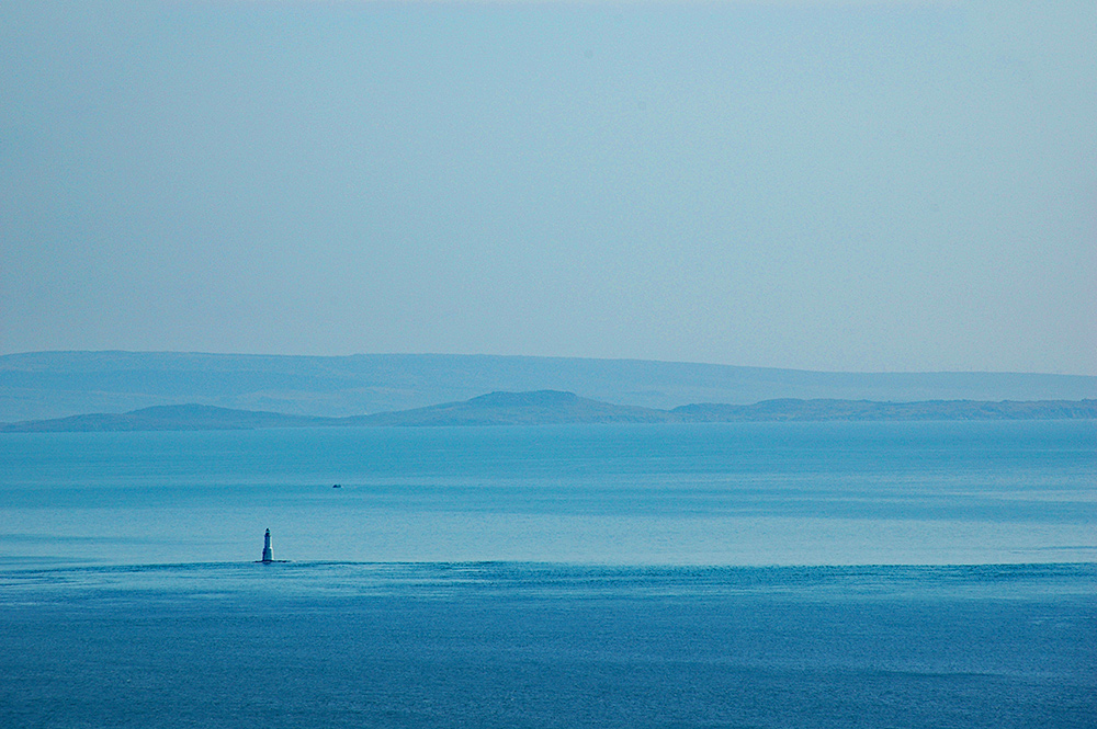 Picture of a lighthouse in a sound between an island and the mainland, another island and the mainland visible in the haze in the distance
