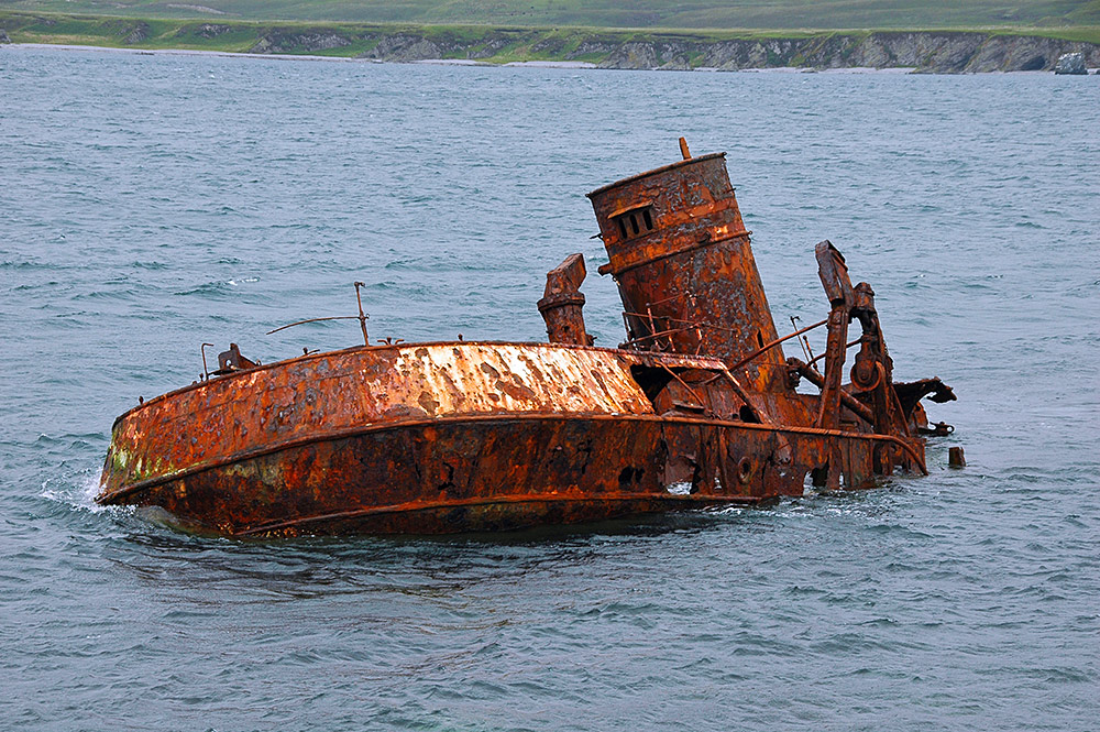 Picture of a rusty wreck low in the water of a sound between two island