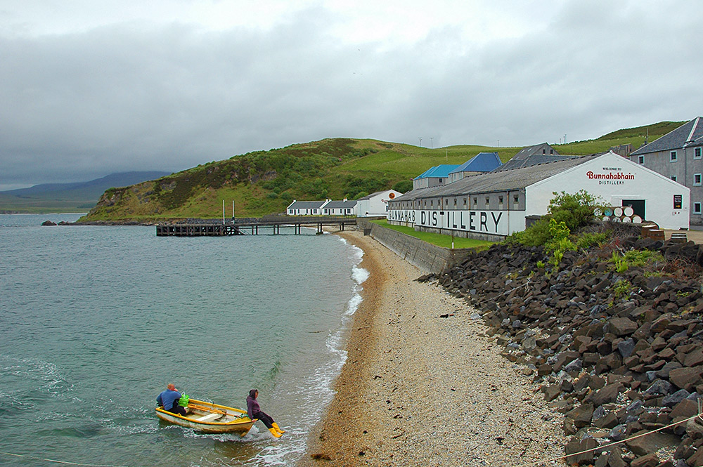 Picture of two fishermen in their dinghy landing on a beach below a distillery
