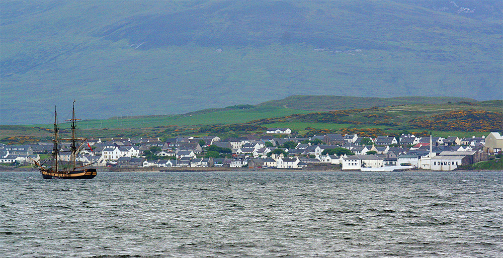 Picture of a tall ship anchored off a coastal village with a distillery (Bowmore)