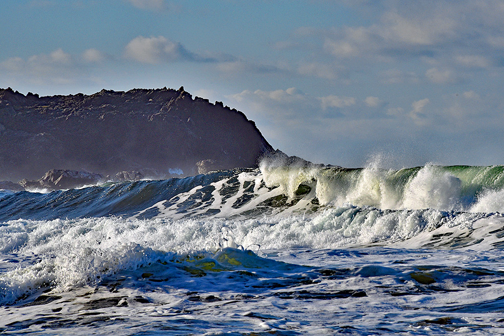 Picture of a big breaking wave with some dark cliffs in the background