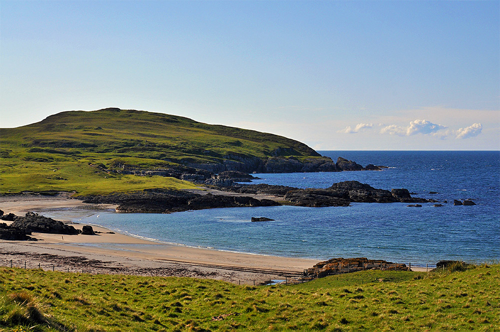 Picture of a bay with a beach and low cliffs surrounded by low hills in some nice June evening sunshine