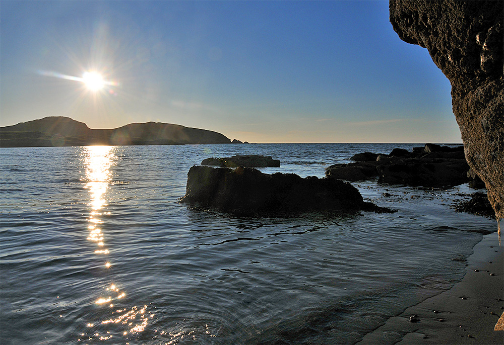 Picture of low sun over a bay with a beach and rocks
