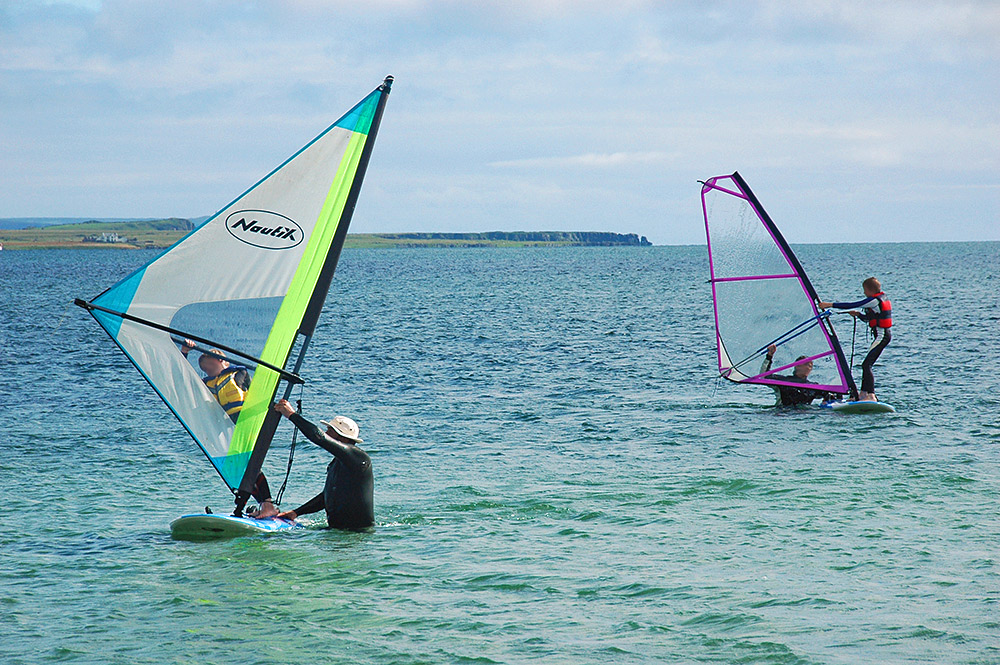Picture of two children learning to windsurf on a sea loch, assisted by two adults