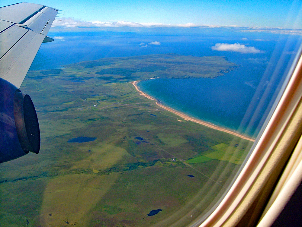 Picture of a view from a plane over a small peninsula next to a wide bay with a sandy beach