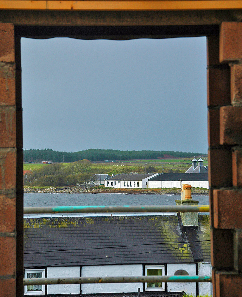 Picture of a coastal distillery (Port Ellen on Islay) seen through a window of an under construction hotel