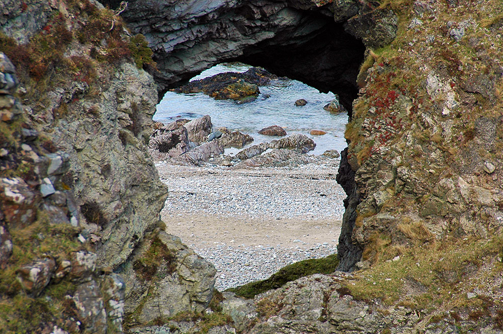 Picture of a large hole in some cliffs, a beach visible through the hole