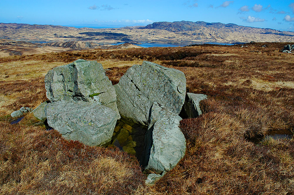 Picture of some boulders on a hillside, a sea loch in the background