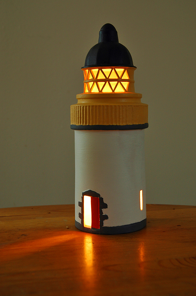 Picture of a lighthouse made out of pottery, a candle lighting it from the inside