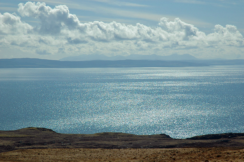 Picture of a view over a sound between an island and the mainland, the sun glistening and reflecting on the water